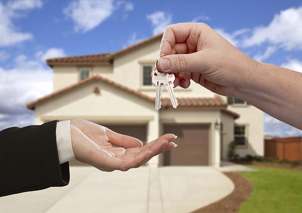 a hand giving keys to another hand in front of a home