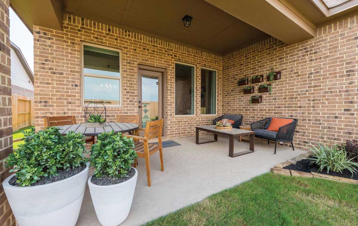 Tall potted plants, a round table surrounded by wood chairs, an outdoor coffee table and paired lounge chairs, and a set of wall-mounted potters bring a warmth and welcoming atmosphere to this modestly sized covered back porch.