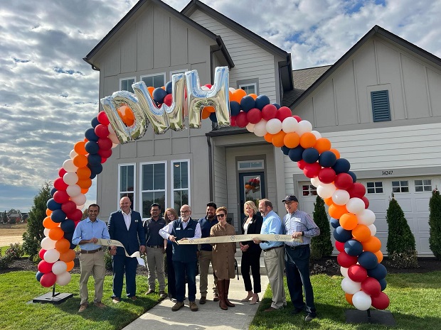 a group of people standing in front of a David Weekley model home holding a large ribbon, there is a large arch of balloons over the people